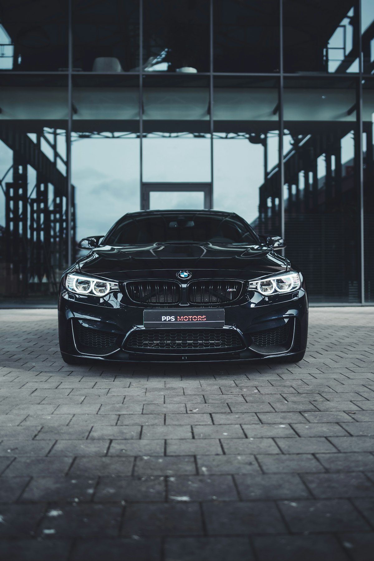 BMW negro estacionado frente a un edificio de cristal en tonos azul acero