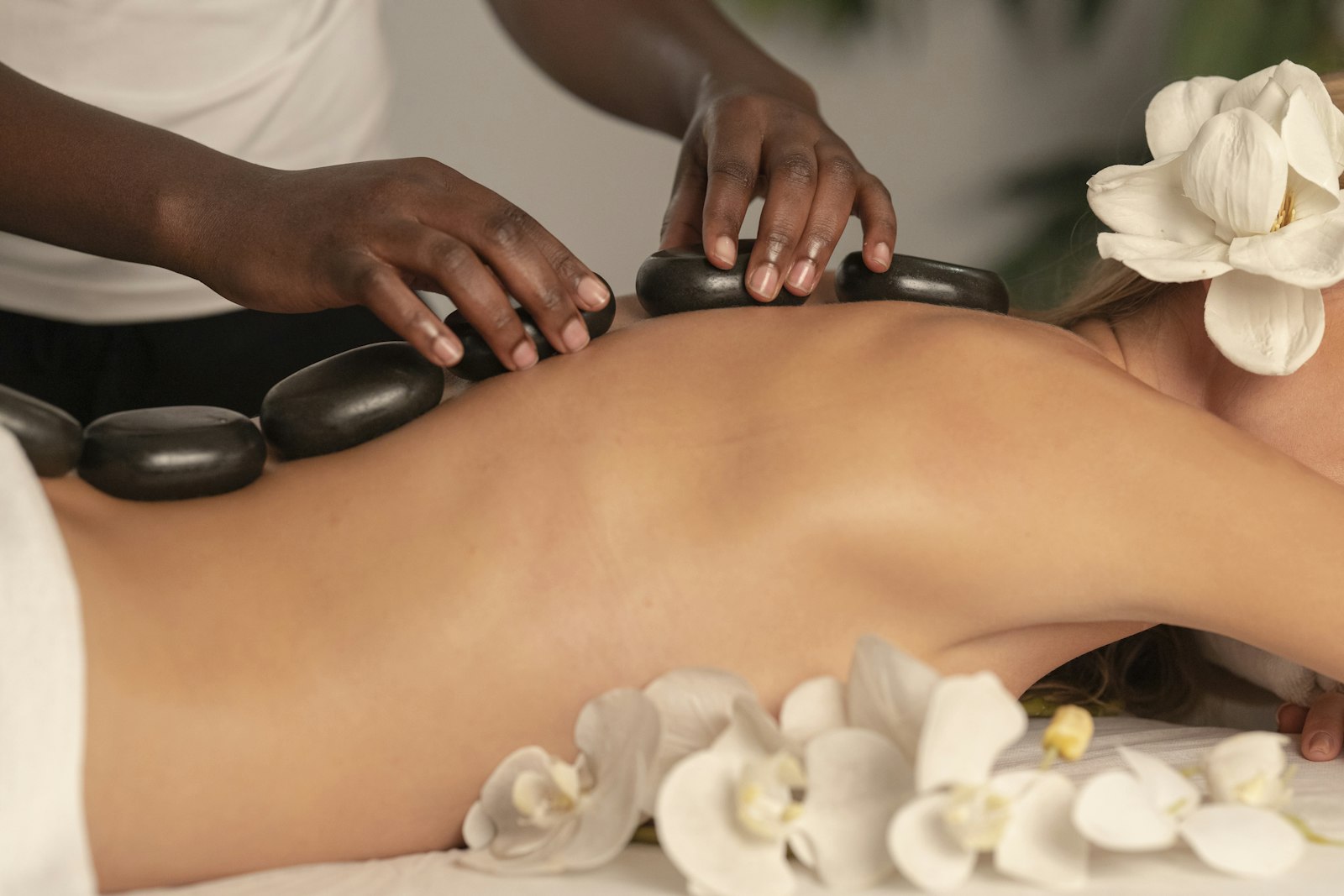 Masaje con piedras calientes y flores blancas en el spa